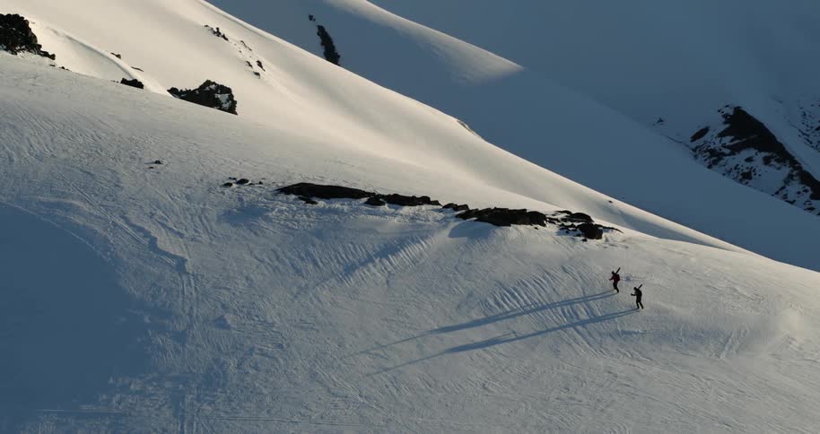 Aerial of two skiers hiking across mountain peak carrying skis