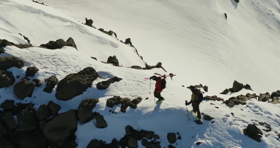 Aerial of two people hiking a rocky mountain ridge holding skis