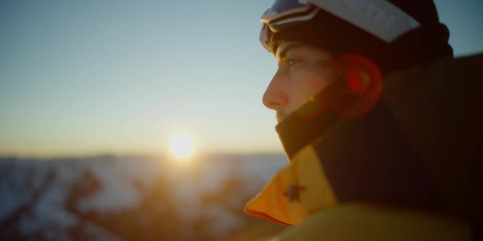 A man stands outdoors in nature and looks around at the mountains