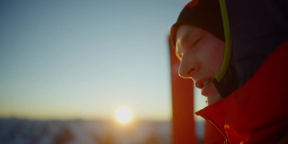 A man with a coat and a hat with skis in the background