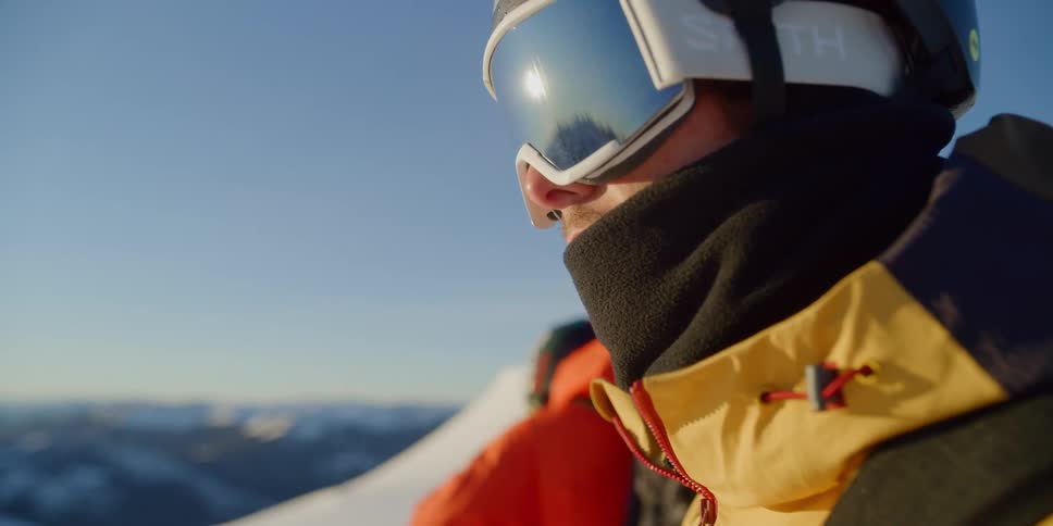 Men in heavy winter gear and snow goggles stand on mountaintop