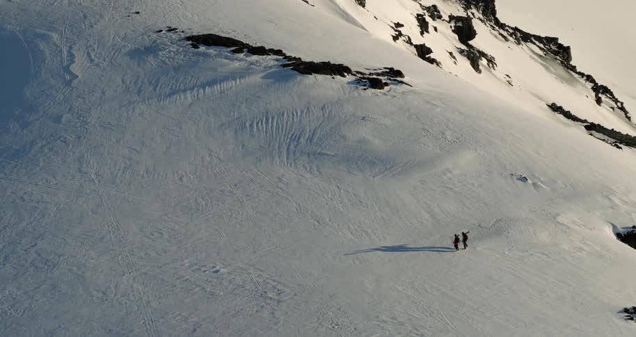 Aerial of skiers hiking across mountain peak carrying their skis