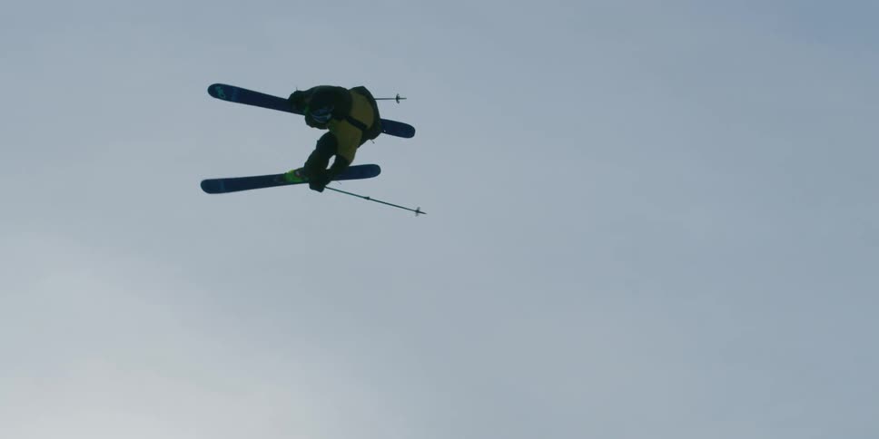A backlit skier jumps and spins through the sky