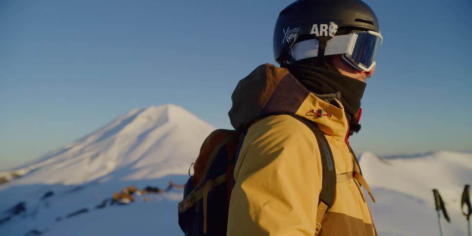 A skier stands at the top of a mountain in front of a volcano