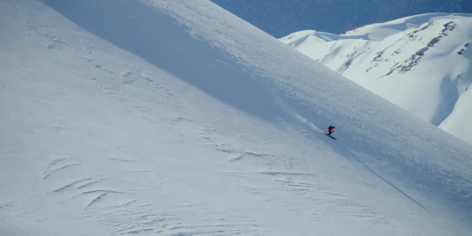 A person skis down a steep mountain ridge in profile