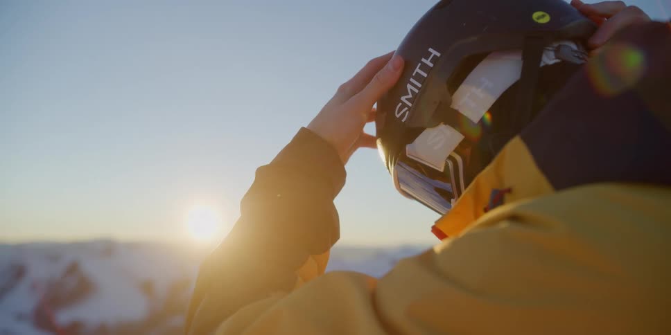 A skier adjusts their helmet at sunrise