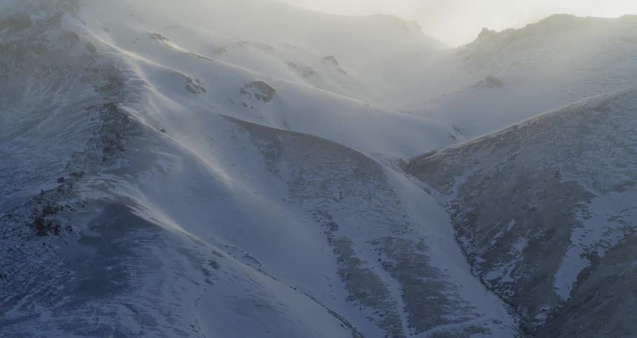 Aerial of snow dusted hills and ridges with sun shining through fog