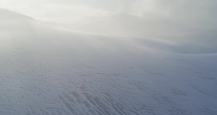 Aerial pull from a snow and mist covered mountain in surreal sunset light