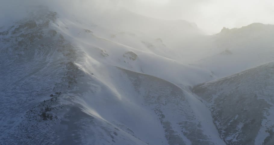 An aerial view of sunset mist floating above snowy mountains in the wilderness