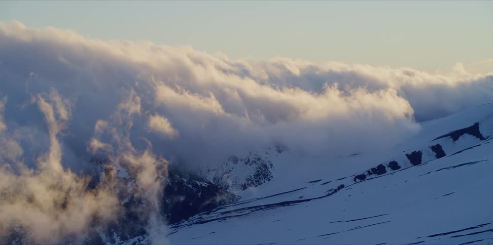 Sunset clouds roll over the snowy slopes of a mountain in timelapse