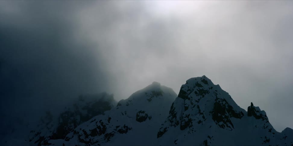 Fog swirling above the peak of a snow capped mountain timelapse