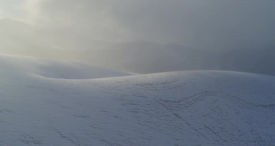 Aerial of snow dusted smooth hills with fog and clouds rolling in