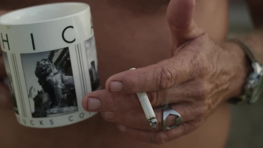 A person is holding a cigarette and a mug