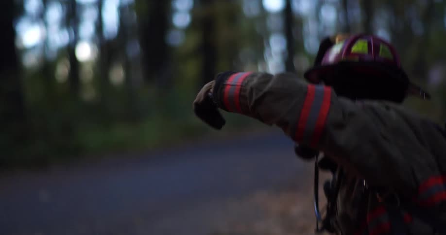 A firefighter with a hose gestures with his arm and hand while in the woods