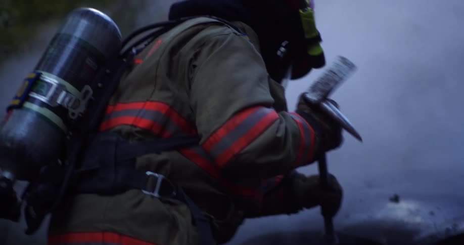 Two firefighters work on a smoking car in the rain