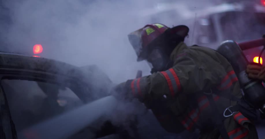 Two firefighters using a hose to put water on a smoldering car
