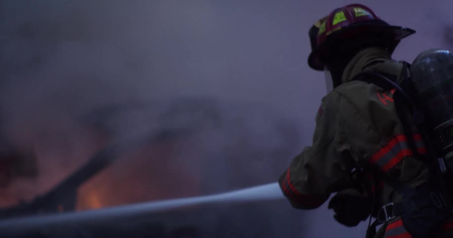 Two firefighters with a hose spraying water on a car that is on fire