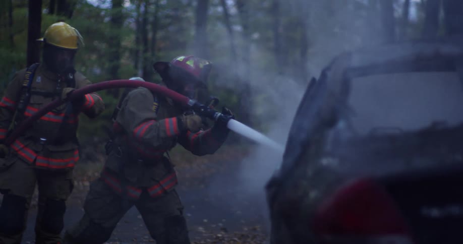 Two firefighters use a water hose on a smoking vehicle