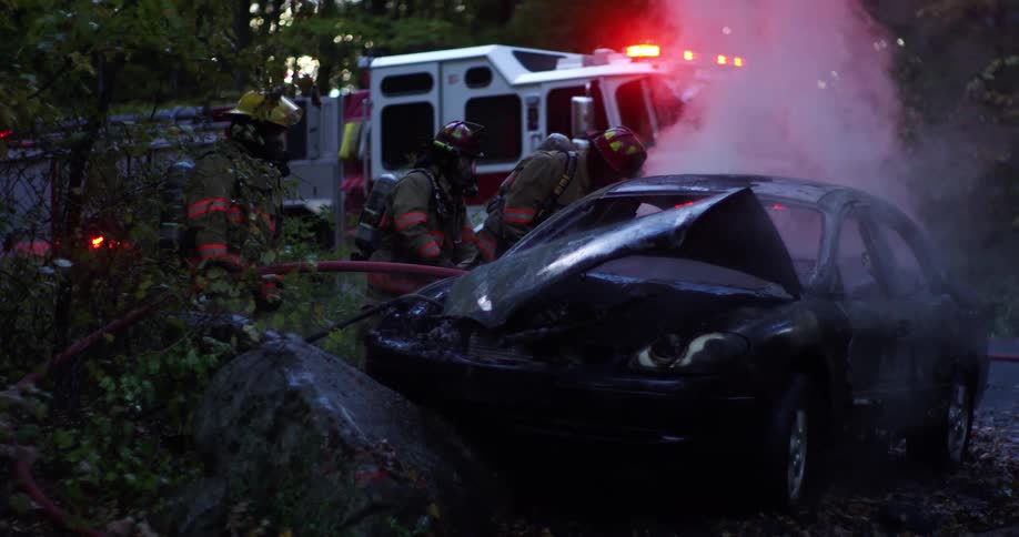 Firefighters look at a crashed car that is smoking