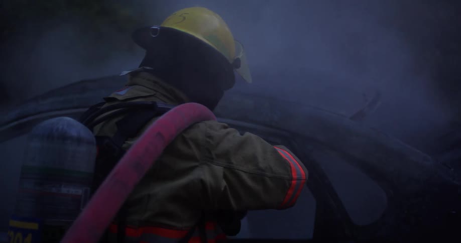 Firefighter sprays burnt car down with fire hose at night