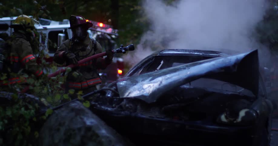 A pair of firefighters readying a fire hose near the smoking wreckage of a car