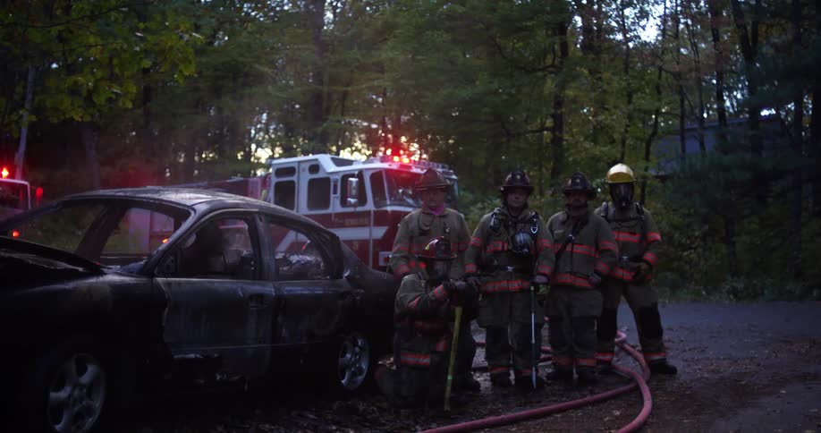 Firefighters pose beside a burned out car that they extinguished with their fire engine parked behind