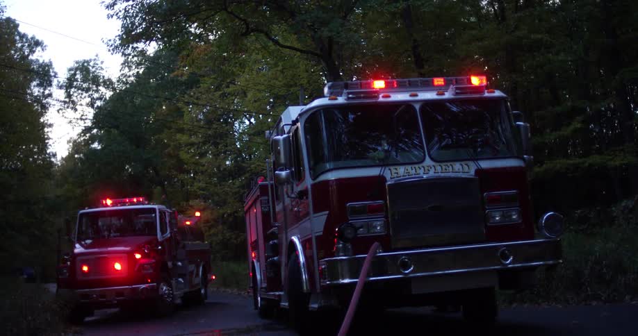 Two firetrucks are parked outside near some trees