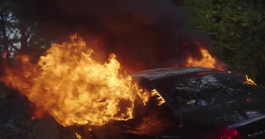A car on fire with trees in the background
