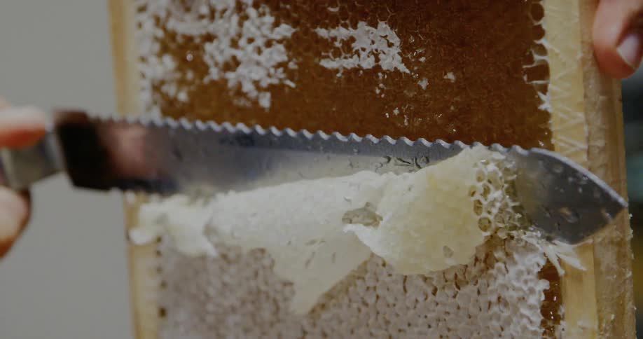 A serrated knife slices off the honey on a honeycomb