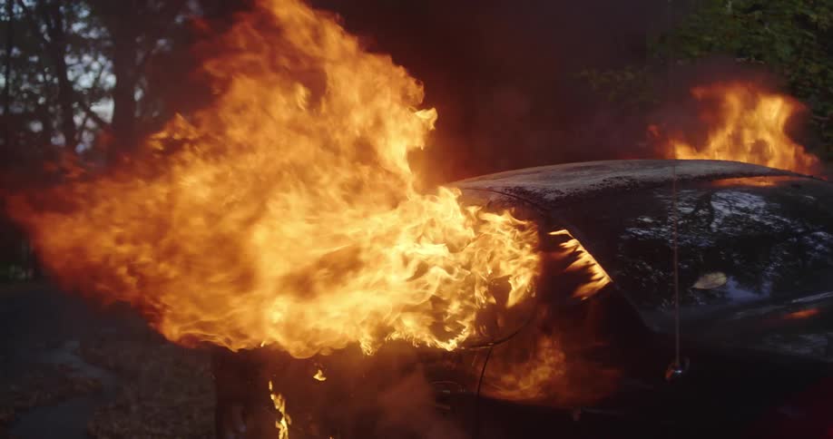 Burning car parked outdoors with flames coming out the windows