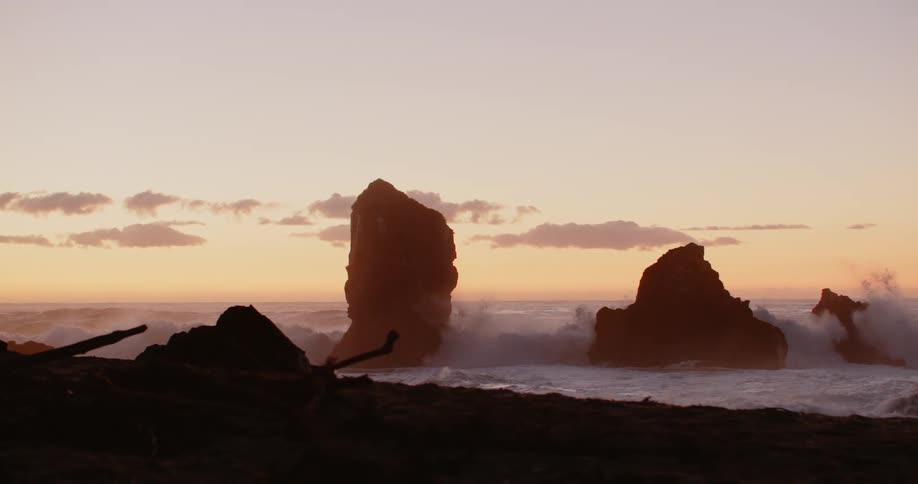 Ocean waves crash on rocks near the shore of a beach at sunset