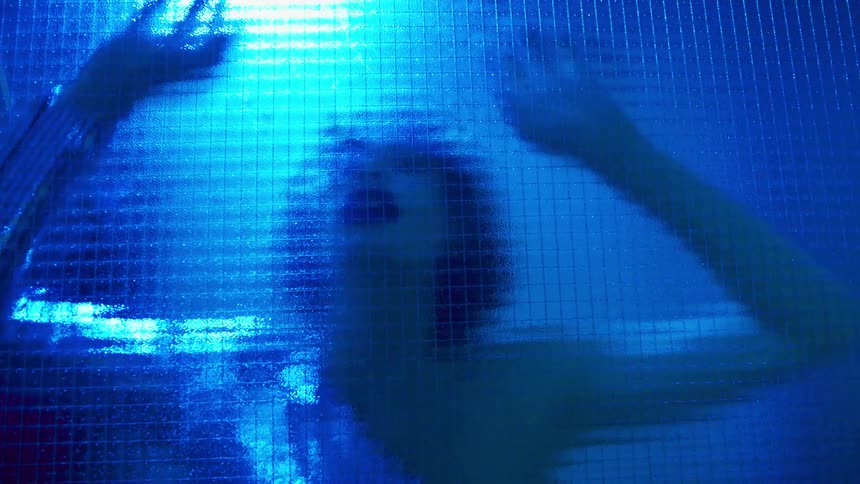 A white woman dances frenetically and throws herself against a semitransparent piece of glass