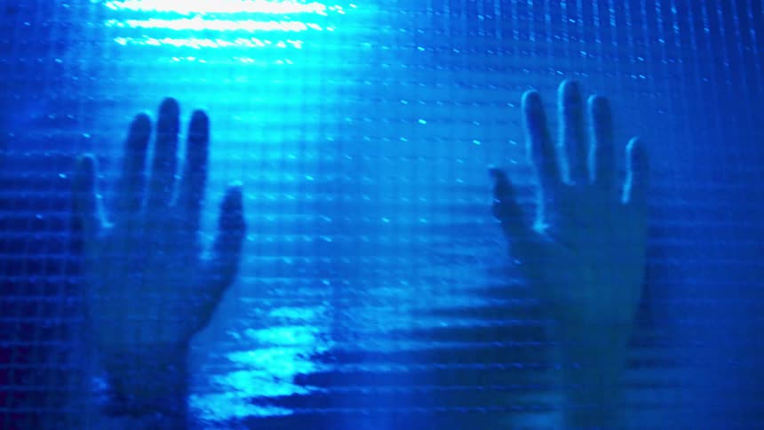 Someone dances behind a glass wall while putting their hands on the glass