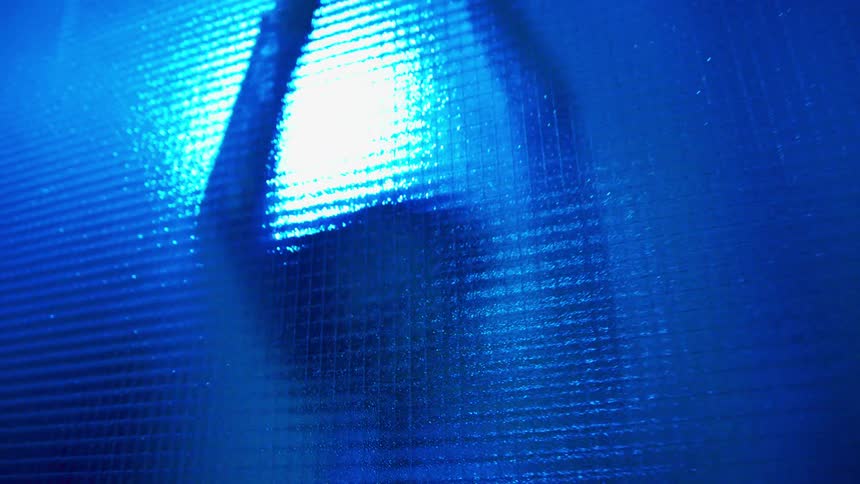 A woman in a silver bodysuit dancing behind a pain of patterned glass