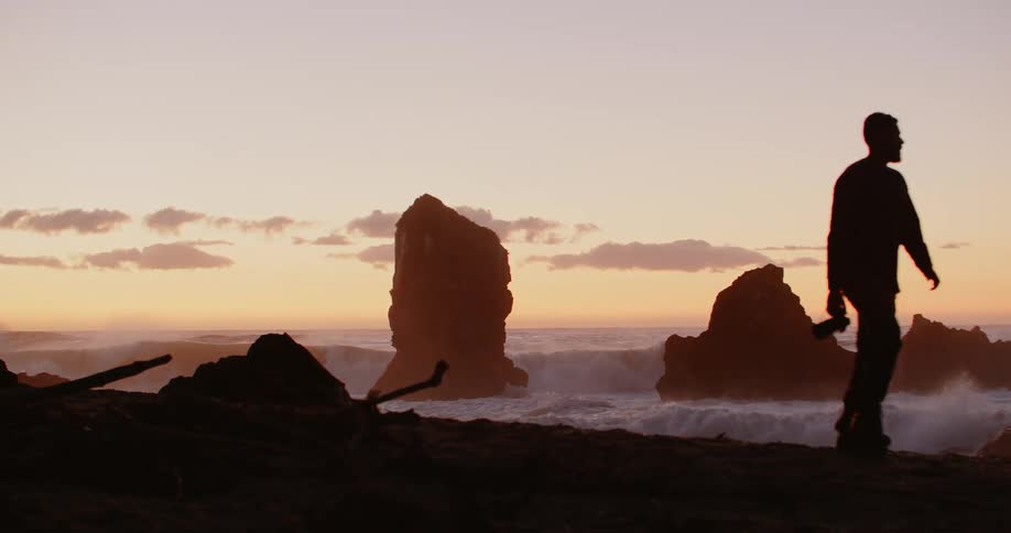 A photographer carries his camera as he walks along the beach