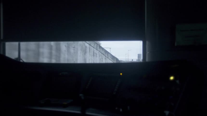 The window of a train car shows the train moving pass a concrete wall barrier