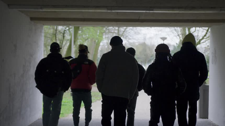 A group of friends walk with hands in pockets through a tunnel onto a park path