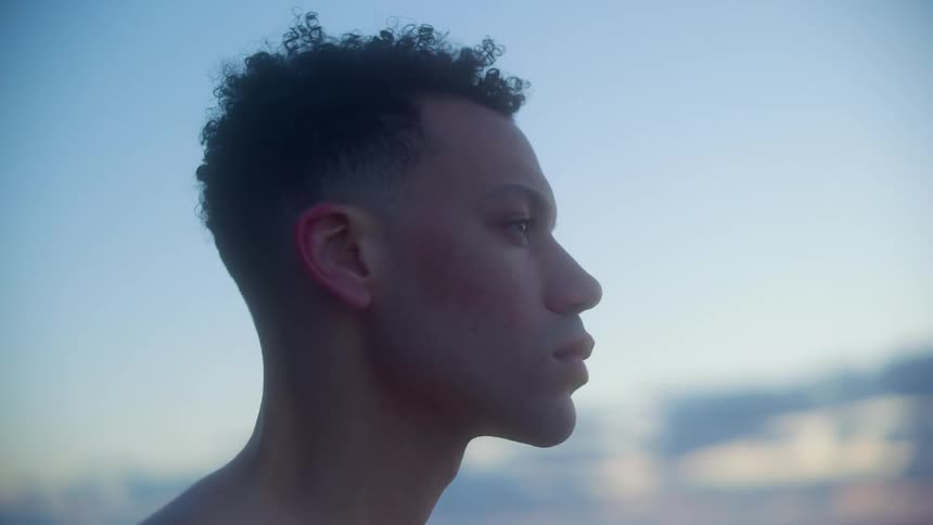 A young man standing expressionlessly outdoors during the day