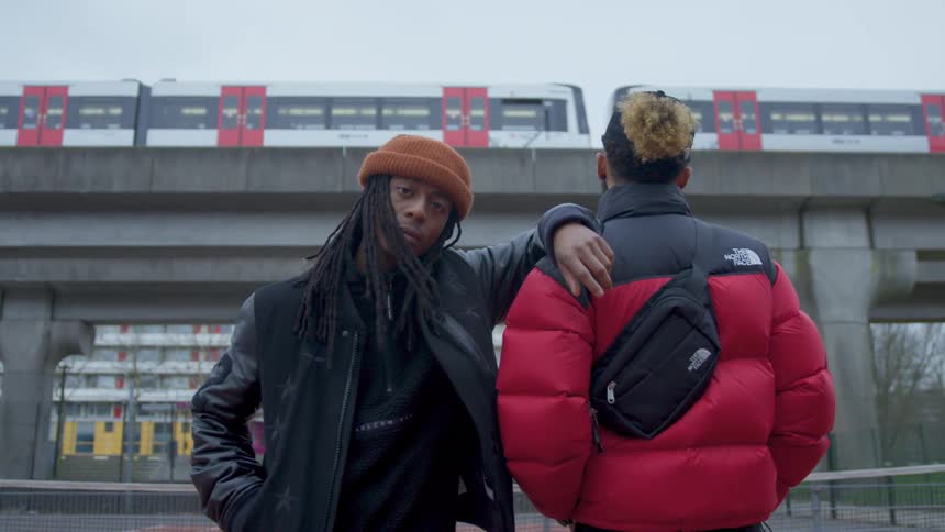 Two men stand outside and one watches a train pass by