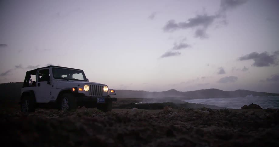 A jeep sits on the shoreline as water splashes to the shore