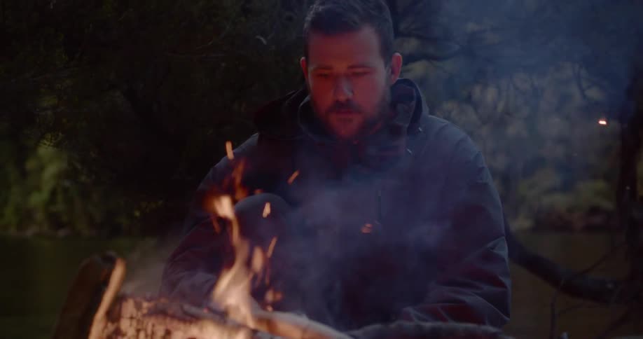 Man sitting in front of campfire near a lake at sunset