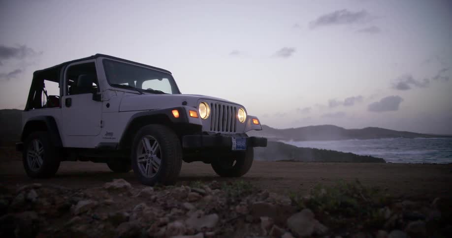 Jeep wrangler parked near coast at sunrise while waves crash on shoreline