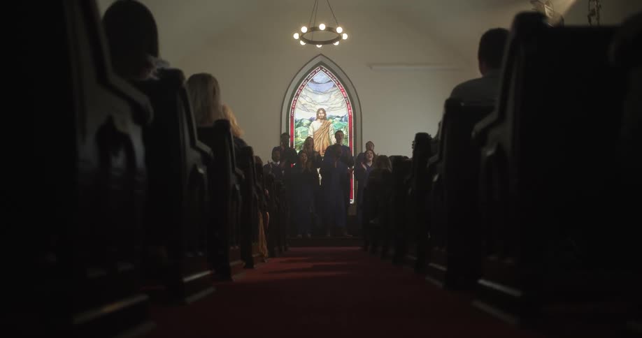 Church choir sings in front of stained glass window in chapel