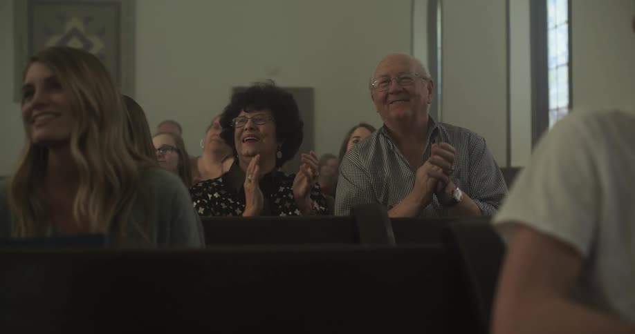 Older couple clapping hands in church pews and smiling