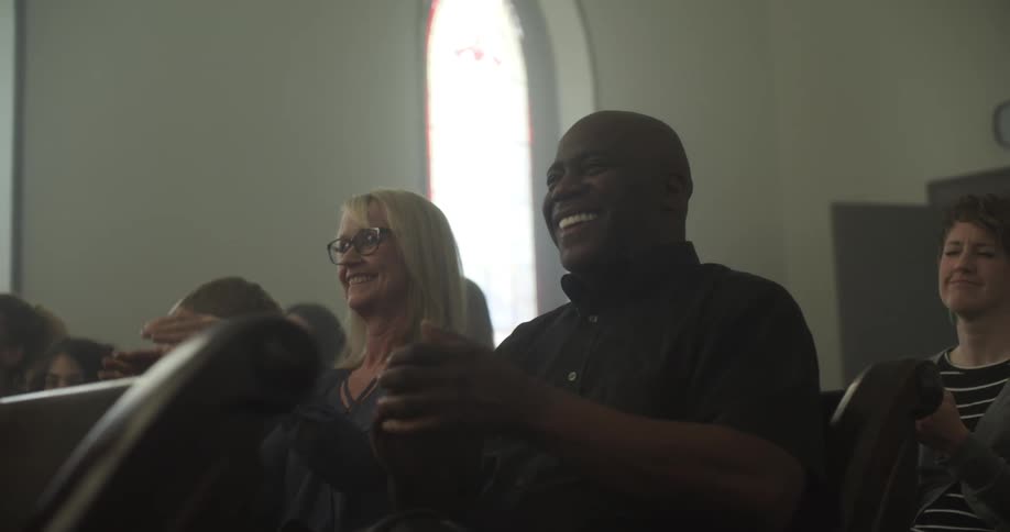 People sitting the pews of a church clapping their hands in rhythm and smiling