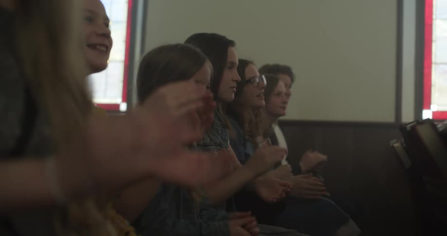 Children and teenagers sit in a pew at church clapping their hands
