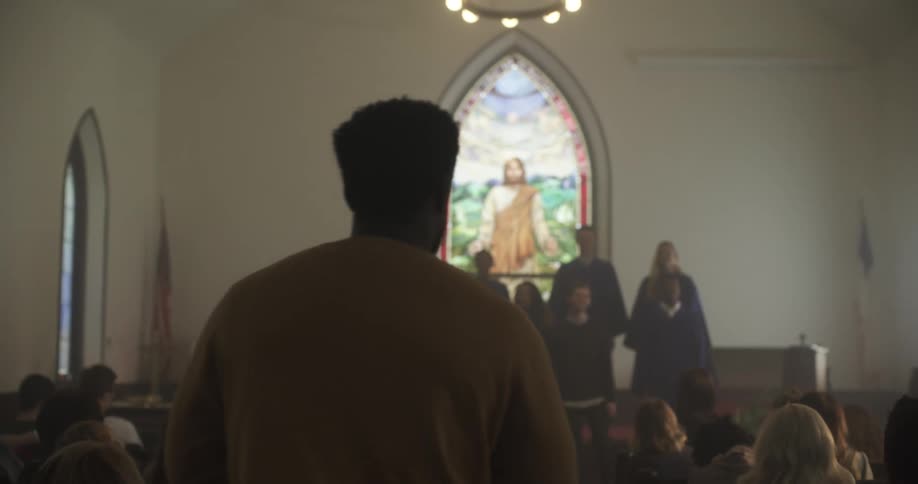 A man walks into a small church as a choir sings up front