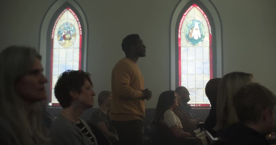 A man walks into a church where people are already seated in pews with his hands folded in front of him