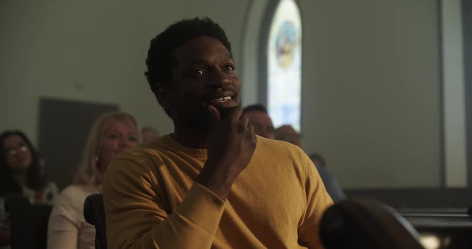 A man sitting in a church pew rubs his face and smiles