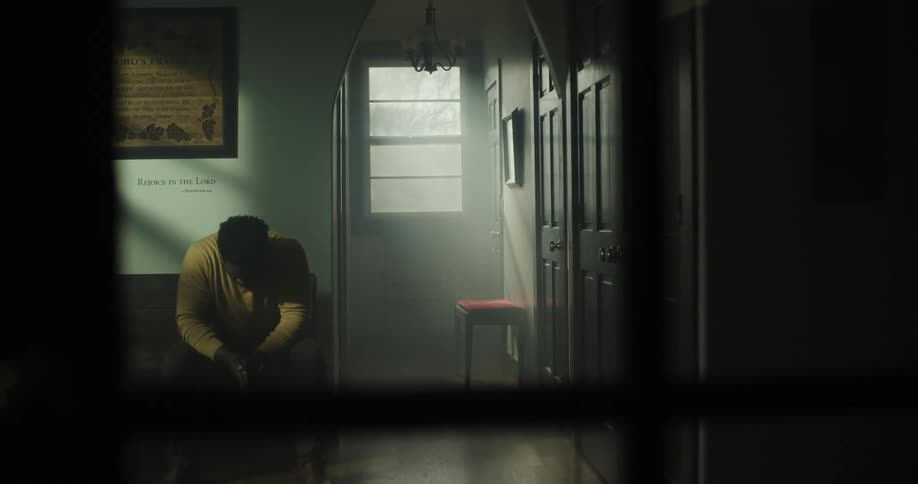 A man sits in a room by himself and puts his head down and rubs his hands together
